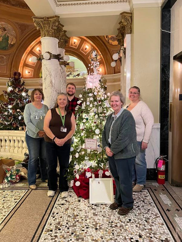 staff pose with decorated tree at South Dakota State Capitol building.