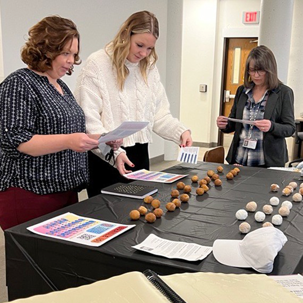 three women look over handouts and table with donut holes arranged in braille