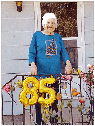 smiling older woman standing at front door with flowers and balloons