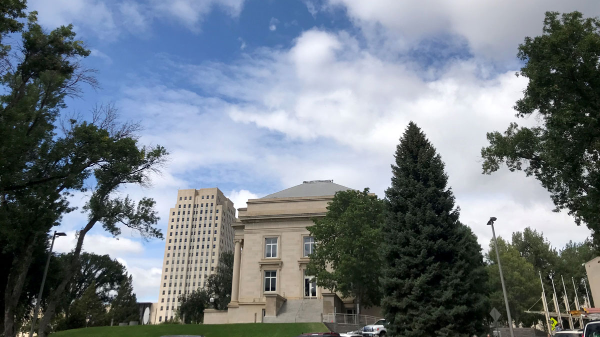 Two story building, surrounded by trees with a 21-story tower in background.