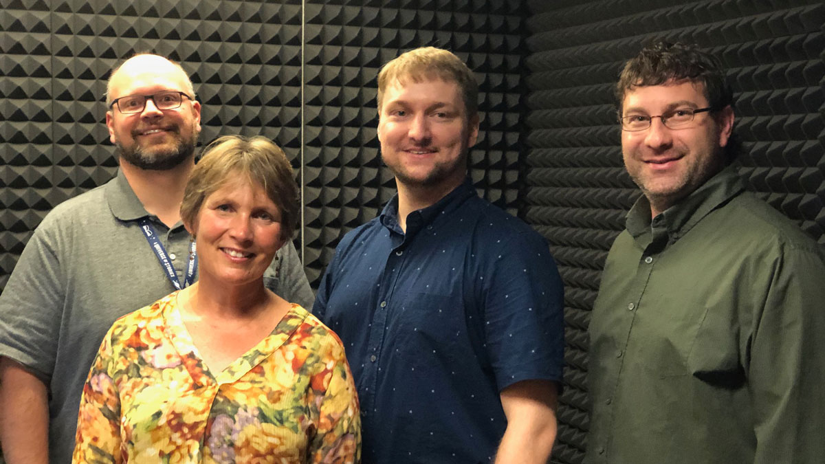 photo of four people standing in recording studio booth.
