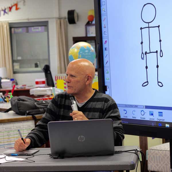 man sitting at computer and drawing tablet in front of screen showing a stick figure human base form
